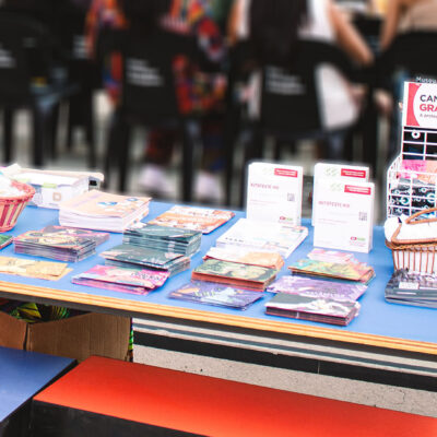 Mesa de ação de saúde pública com panfletos informativos sobre ISTs e prevenção, testes rápidos de HIV e cestas com preservativos gratuitos disponíveis para retirada. Foto: Luiz F. Petty